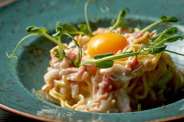 Appetizing italian pasta carbonara with yolk, white sauce and bacon in a blue plate on a wooden background