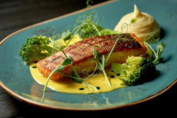 Salmon steak with yellow sauce, vegetable puree and broccoli. Wood background
