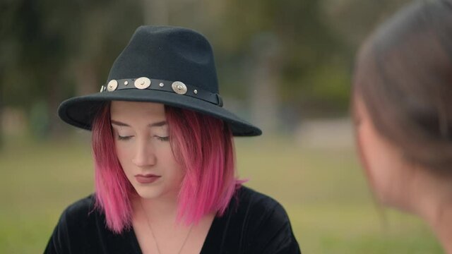 nice pink haired girl using a black hat talks to another girl. close up, over the shoulder shot
