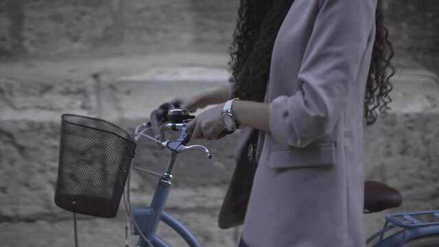 Cropped Image Of Curly-Haired Female Wearing Casual Clothes Is Walking With A Bicycle. Tracking