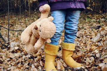 A child in bright rubber yellow boots stands and holds a teddy bear's paw in his hand. Stuffed toy,...