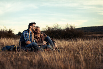 Naklejka na ściany i meble Couple sitting on grass during sunset resting after hiking.
