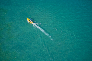 Yellow high-speed luxury boat with people moving on turquoise water. Boat performance fast movement on clear water aerial view.