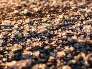 Salt grains on icy sidewalk surface in the winter. Applying salt to keep roads clear and people...