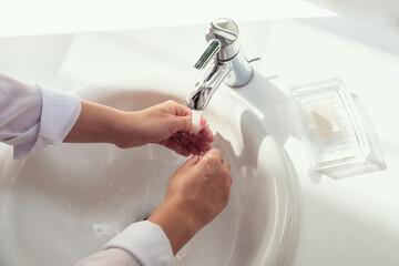 Woman washing hands rubbing with soap in white sink in bathroom with sunlight from the window. Protection from bacteria and virus. Hygienic concept. Top view