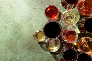 Red, white and rose wines in assortment in glasses on green background, top view. Wine bar, shop, winery, wine tasting concept. Hard light copy space