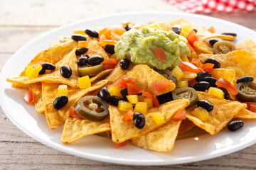 Mexican nachos tortilla chips with black beans, guacamole, tomato and jalapeno on wooden table