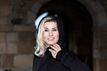 portrait of blonde woman dressed in black looking at camera with a hood on