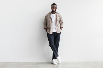 Handsome young black man in casual wear looking at camera and smiling, standing against white...