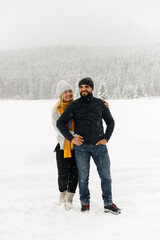 Fototapeta na wymiar Attractive man and woman cuddling in the frosty forest. Adult couple in sweaters have fun on walk. Romantic date in winter time.Winter lovestory