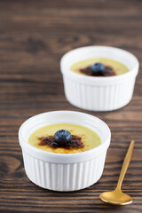 Homemade creme brulee with blueberries in bowls on a wooden table.