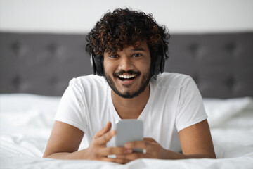 Cheerful hindu guy with wireless headset and smartphone