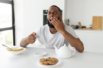 Black man yawning, pouring coffee away from cup - obrazy, fototapety, plakaty