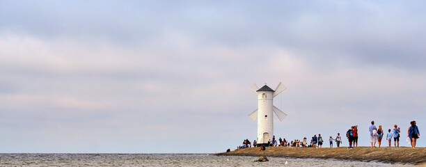 Tourists walk on the pier to a lighthouse on the Baltic Sea in Swinoujscie in Poland. With blurred cloudy sky in the background.