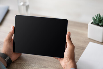 Cropped young african american male hold tablet with blank screen, work, watch video, chatting on desk in home