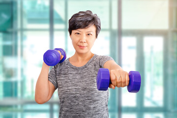Active senior older Asian attractive elder woman training, exercising, workout at the gym in a health club with lifting weights dumbbells. Older senior adults exercise at fitness gym club ideas