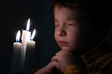 Little cute boy praying in front of a burning candle