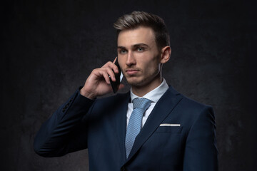 Naklejka premium Young business man in a suit and tie talking on a mobile phone on a black textured background communication concept.