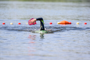 Swimmer swimming outdoor in nature with a green swimming cap and orange buoy