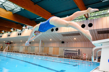 Female swimmer dives into the indoor swimming pool wearing a blue swimsuit
