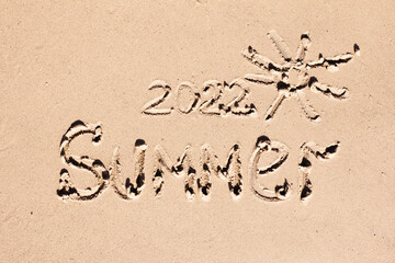 The inscription 2022 and the word summer are drawn on the light sand. New Year symbol, calendar, summer concept
