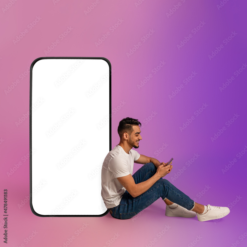 Poster cheery arab guy sitting near big cellphone with blank screen, using mobile device, using new app in 