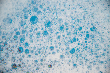 Abstract background texture of white soap foam. Shampoo foam with bubbles on a blue background.