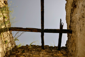 Ancient dilapidated stone structure with remains of wooden beams. Grass grows on walls. Bottom view, against blue sky.  Copy space. Selective focus.