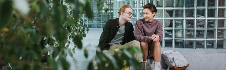 Young tourists talking near backpack and plants in hotel, banner