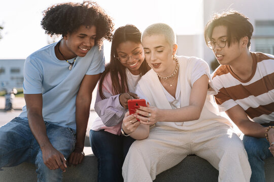 Group of gen z friends sitting together using mobile phones to share content on social media