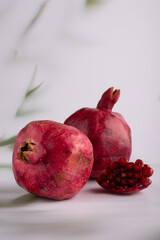 Simplicity in elegance with two whole pomegranates on a pristine white surface, their skins glowing and one cluster of ruby seeds lying beside.