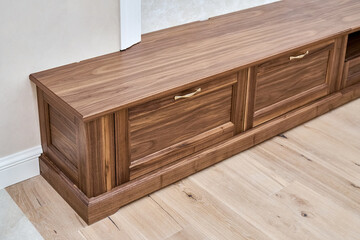 Elegant new TV cabinet made of veneer and solid walnut lumber with gold handles near wall in light room close upper view