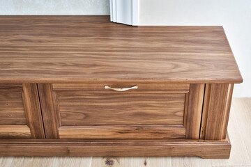 Elegant new TV cabinet made of veneer and solid walnut lumber with gold handles near wall in light room close upper view