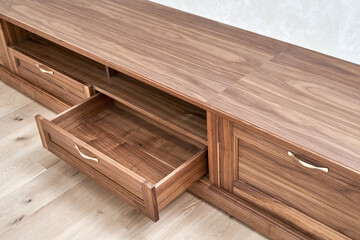 Elegant new TV cabinet made of veneer and solid walnut lumber with gold handles near wall in light room close upper view