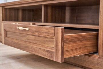 Elegant new TV cabinet made of veneer and solid walnut lumber with gold handles near wall in light room low angle view