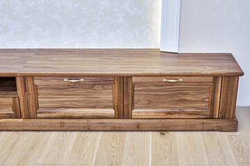 Elegant new TV cabinet made of veneer and solid walnut lumber with gold handles near wall in light room close upper view