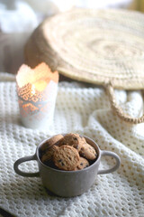 Bowl of chocolate chip cookies, soft knitted basket, wicker basket and candle holder with lit candle. Hygge at home. Selective focus.