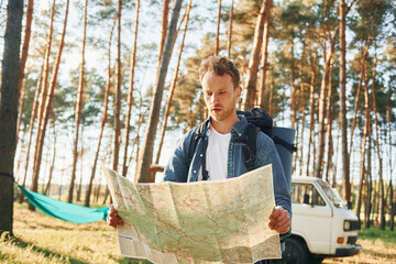 Uses map. Man is traveling alone in the forest at daytime at summer
