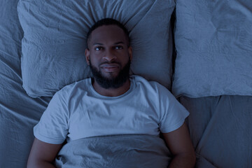 Black man lying in bed and thinking in the night