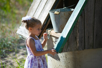 Surprised pretty little girl in country style staying near to well. High quality photo © Anastasia