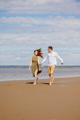Fototapeta na wymiar a couple of a man and a woman are walking on the beach or running along the sand along the seashore. beautiful and young European man and woman on a romantic walk in nature, a couple in love, a happy