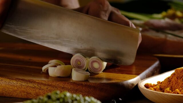 A Closeup view of chef cutting lemongrass in chopping board with ingredient in kitchen background 