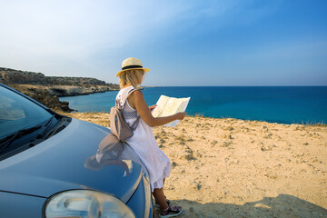 A beautiful and stylish woman is traveling by car. Mature female traveler travel  by car, look at the road map against the sea, Cyprus.