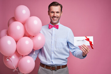 Caucasian mature man holding pink balloons and a gift card