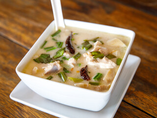Tom kha kai in ceramic bowl on wooden table. Tom Kha Gai is Thai traditional spicy, sour and hot soup with coconut milk. Thai and Lao cuisines.