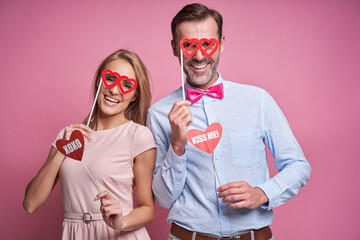 Caucasian couple at Valentine's Day posing on pink background with photo booth accessories