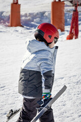 Fototapeta na wymiar Boy in grey and black ski clothes with a red helmet climbing the mountain with the material to descend
