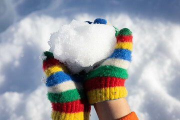 Two children hands with wool gloves holding a snowball