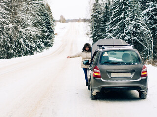 beautiful girl near the engine of a broken car on a winter snowy road. froze and calls for help