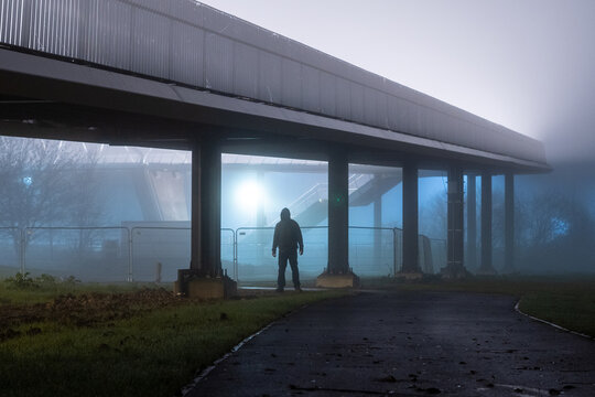 A Scary Hooded Man Standing Under A Bridge At Night